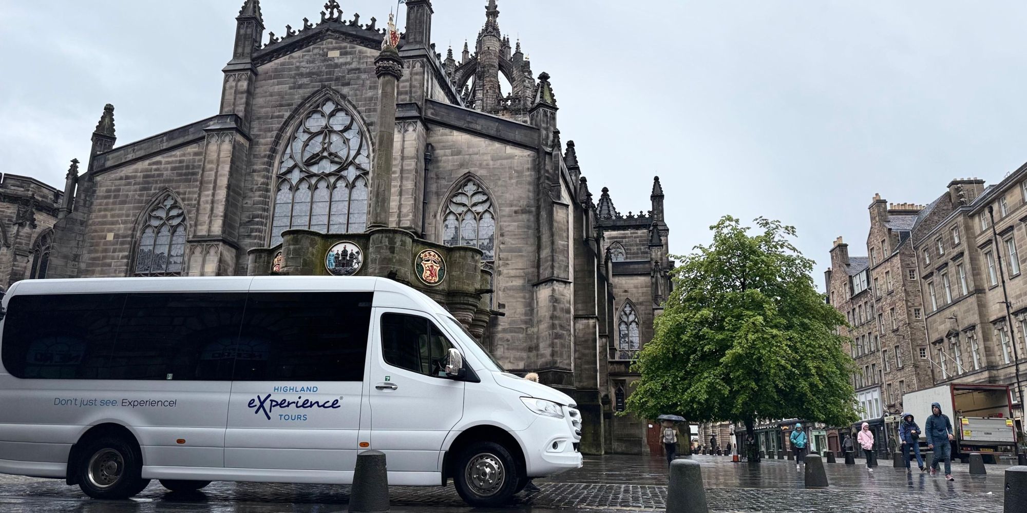 White tour bus in front of a historic cathedral on a rainy day.