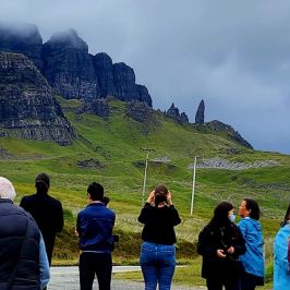 Group of people standing in front of a grassy mountain landscape with cloudy sky.