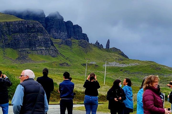 Group of people standing in front of a grassy mountain landscape with cloudy sky.