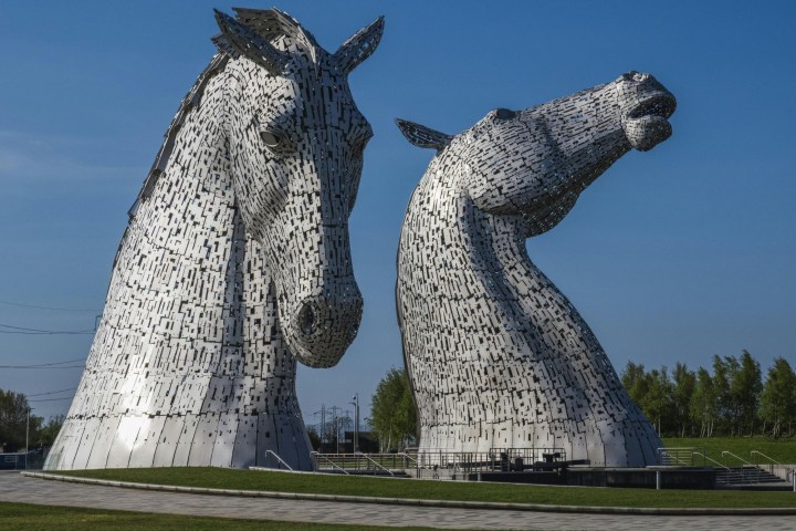 Two large, metallic horse head sculptures under a clear blue sky.