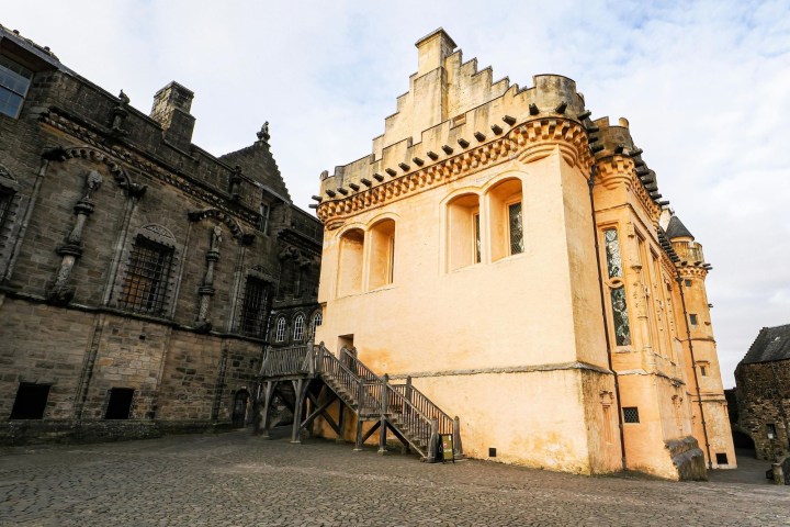 Historic stone and yellow buildings with ornate details and a cobblestone courtyard under a cloudy sky.