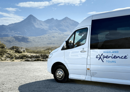 White tour van parked with mountains in the background, labeled 'Highland Experience Tours'.