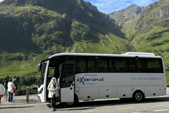 Tour bus and people with mountains in the background under a blue sky.