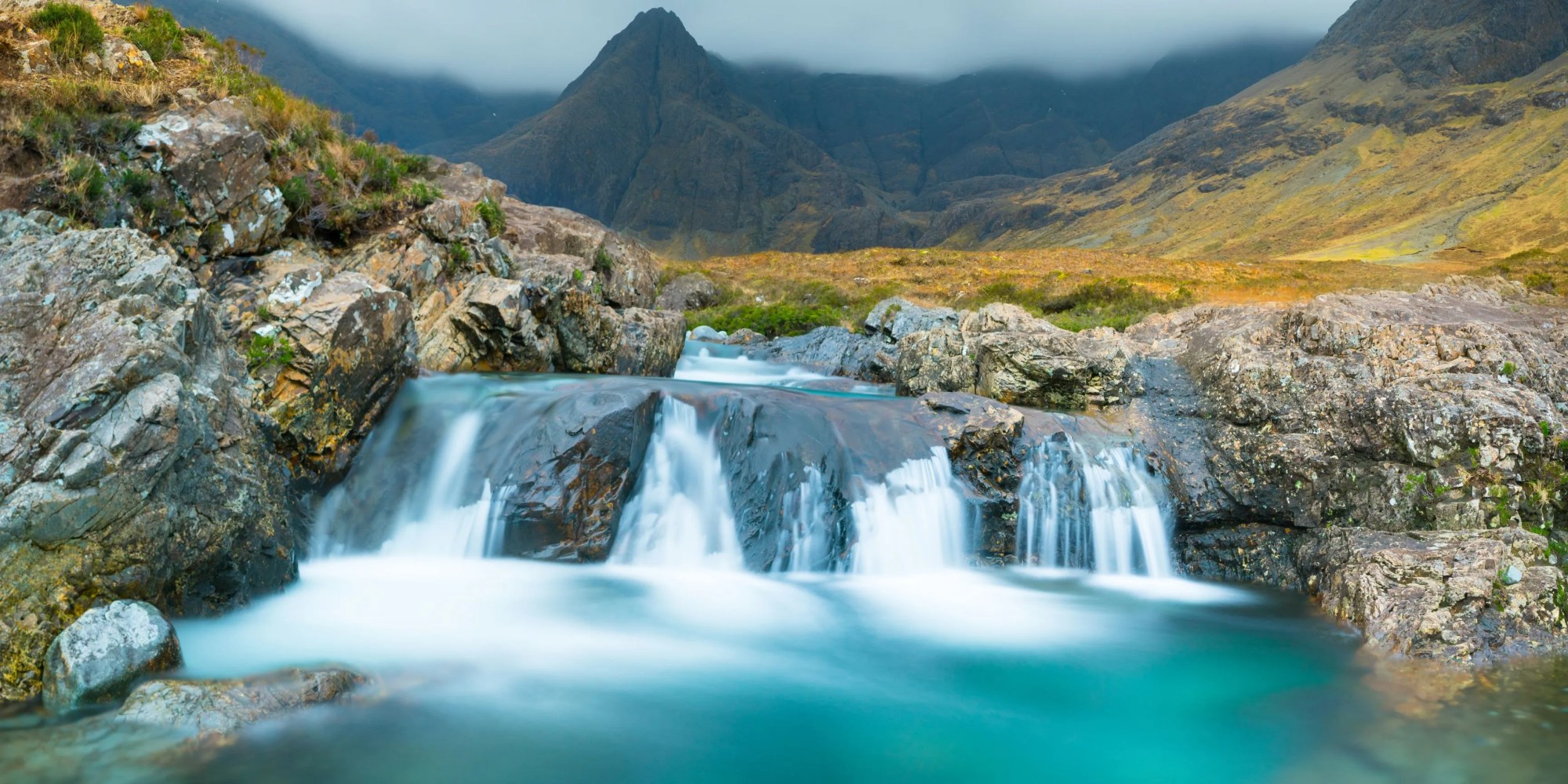 Small waterfall flowing over rocks with mountains in the background.