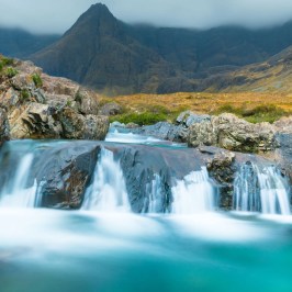 Small waterfall flowing over rocks with mountains in the background.