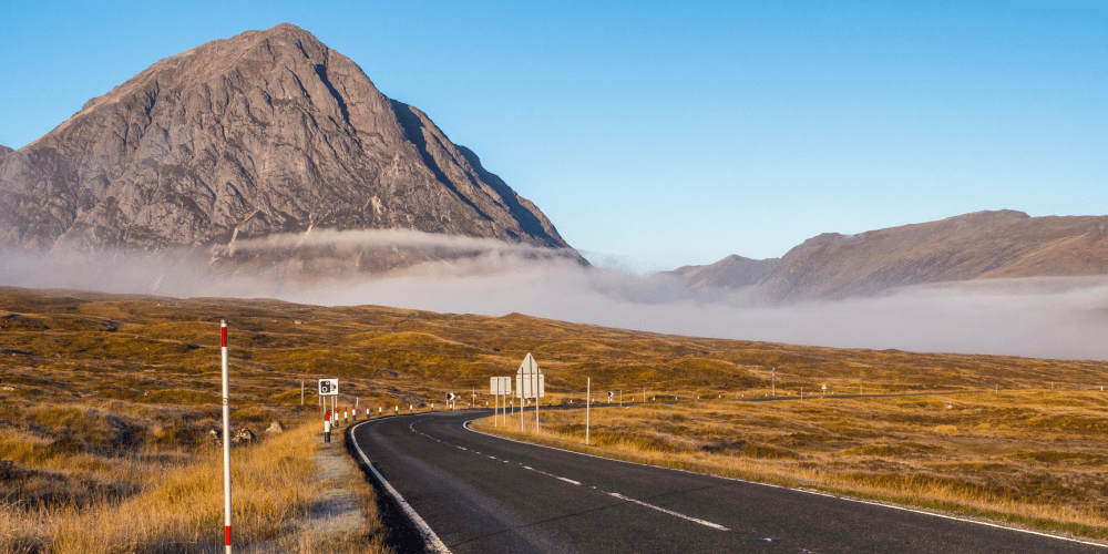 Road leading to a large mountain with fog and clear sky in the background.