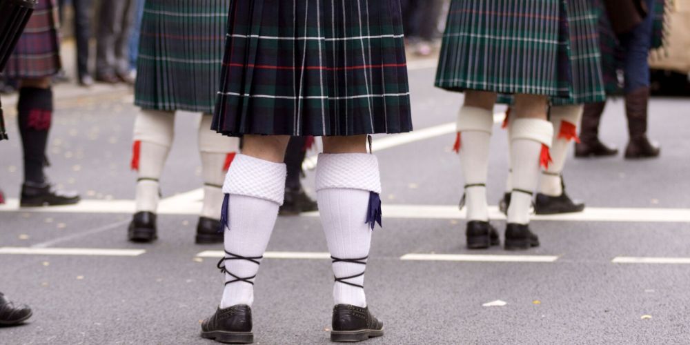 People wearing kilts and knee-high socks walking on a street.