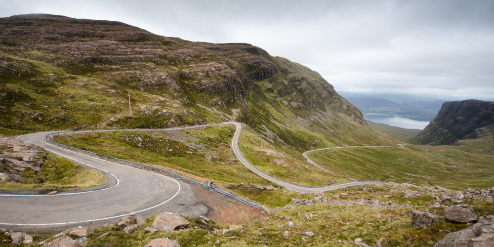 Winding road through mountainous landscape under cloudy sky.