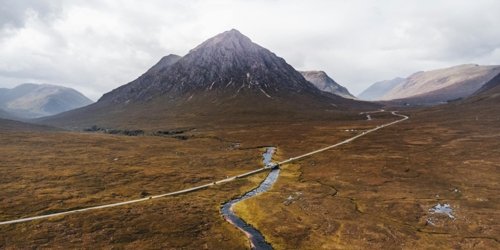 Aerial view of a mountain with a road and stream in the foreground.