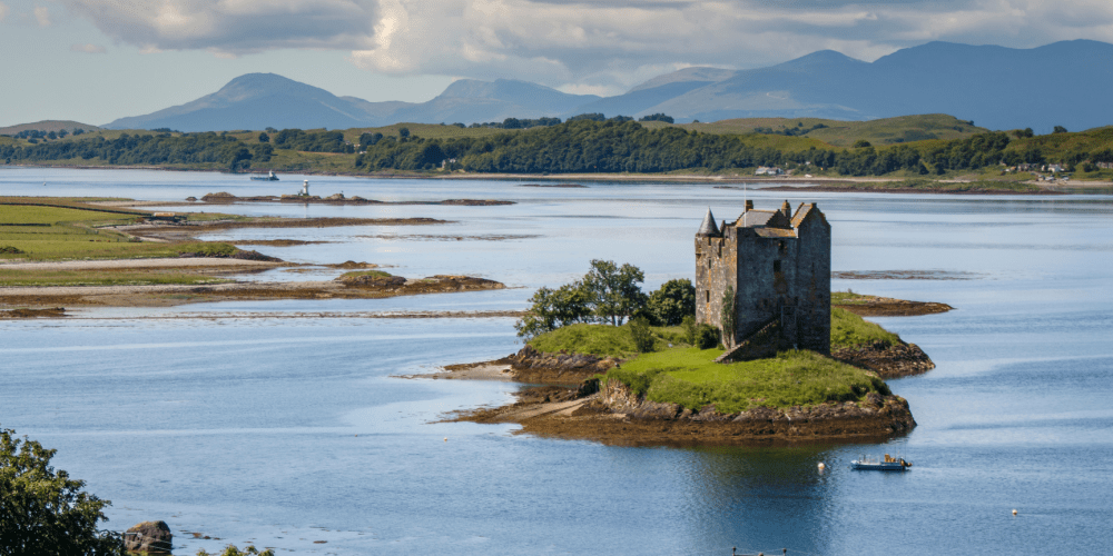 Castle on small island in a lake with mountains in the background.