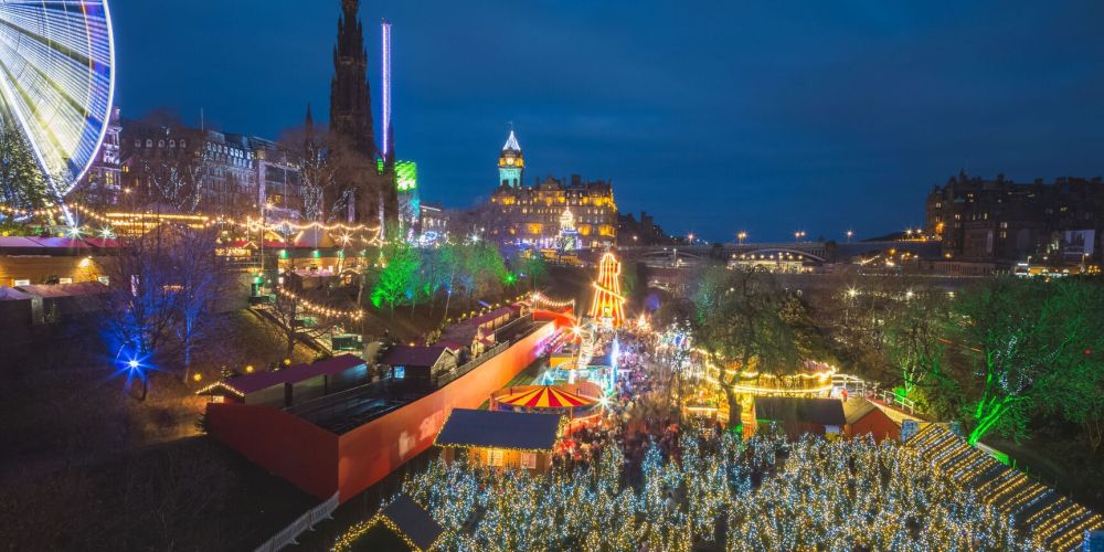 Festive cityscape with lit-up buildings, ferris wheel, and holiday lights at night.