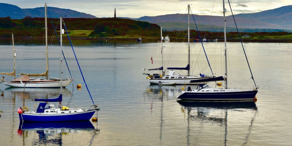 Four sailboats anchored on calm water with hills in the background.
