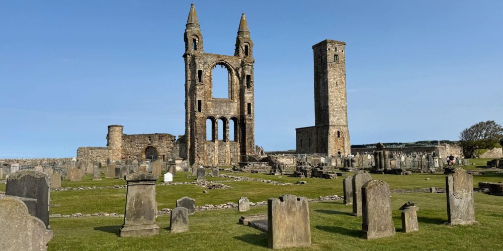 Old cathedral ruins with tombstones in a grassy graveyard.