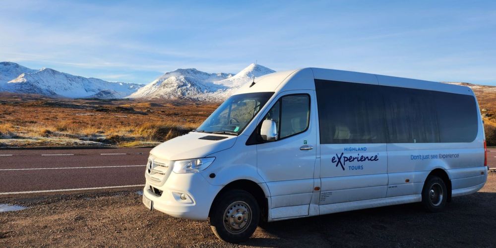 White tour van parked on road with snow-capped mountains in the background.