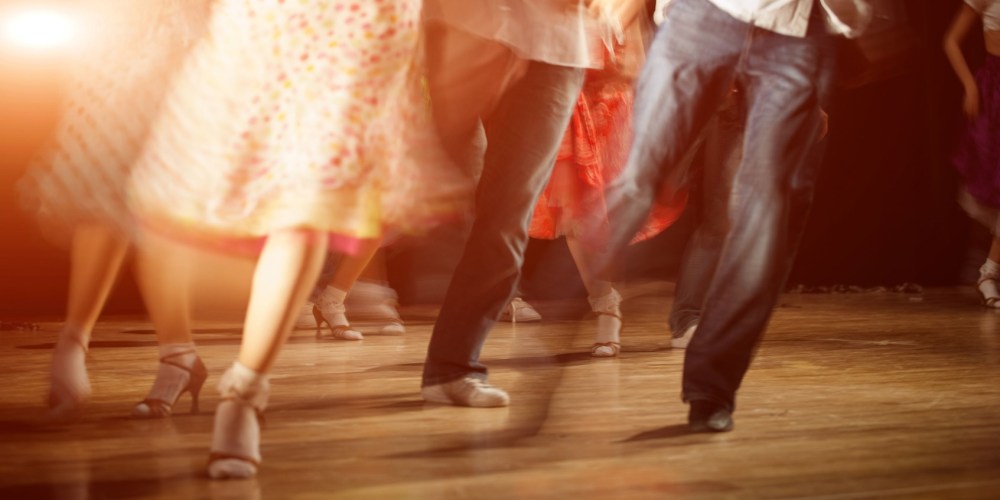People dancing energetically on a wooden floor with blurred motion and warm lighting.
