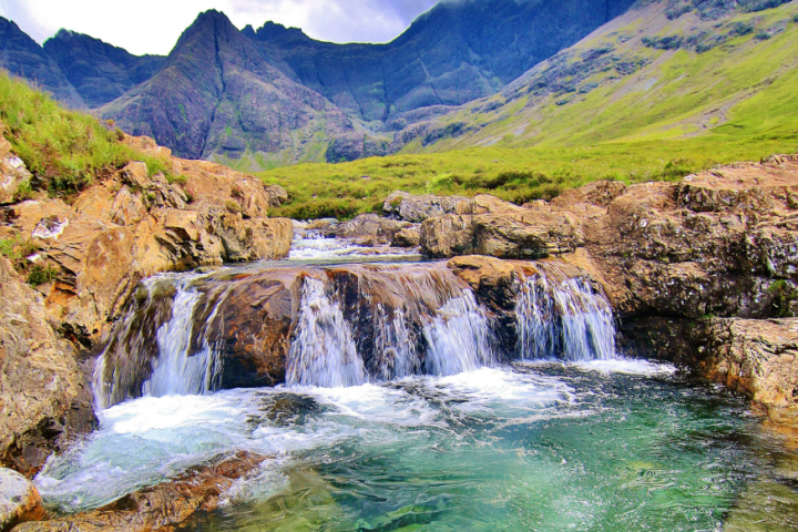 Small waterfall cascading over rocks with mountains in the background.