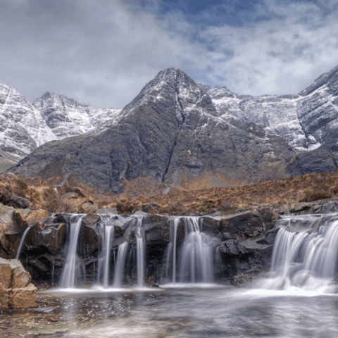 Snowy mountain with waterfall cascading over rocks in foreground.