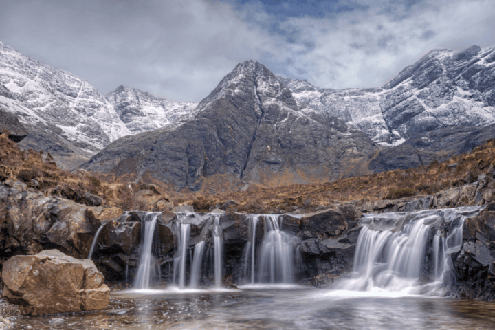 Snowy mountain with waterfall cascading over rocks in foreground.