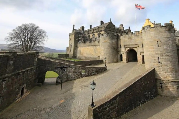 Stone castle with tower, flag, and archway entrance on a sunny day.
