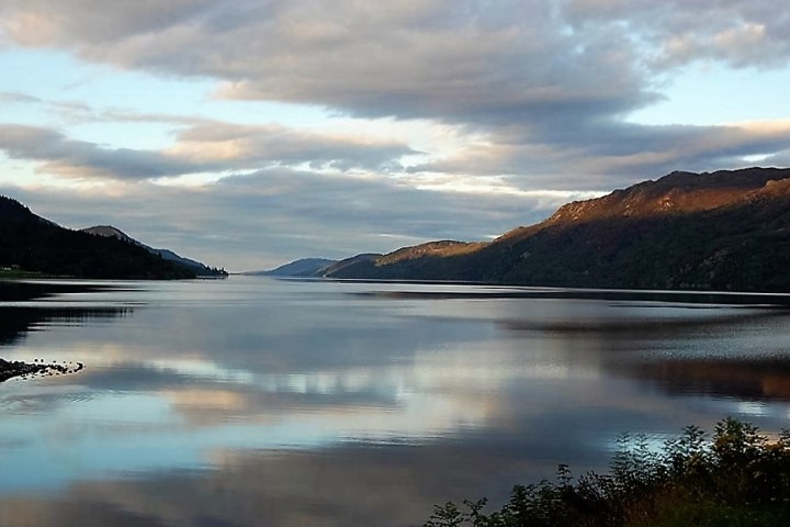Calm lake reflecting clouds and mountains during sunset.