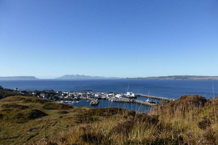 Coastal town with a marina, hills, and clear blue sky.