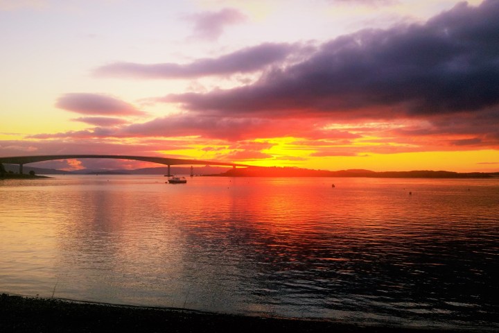 Sunset over water with bridge silhouette and vibrant orange sky.