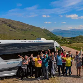Group of people posing by a white tour van in a scenic mountainous landscape.