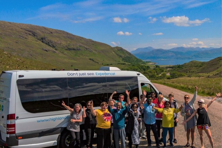 Group of people posing by a white tour van in a scenic mountainous landscape.