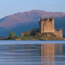 Castle surrounded by water with mountains in the background at sunset.