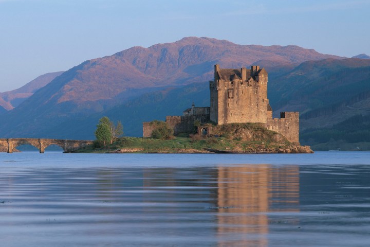 Castle surrounded by water with mountains in the background at sunset.