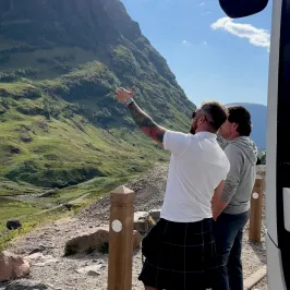 Two men stand by a road, one pointing at a mountain landscape.