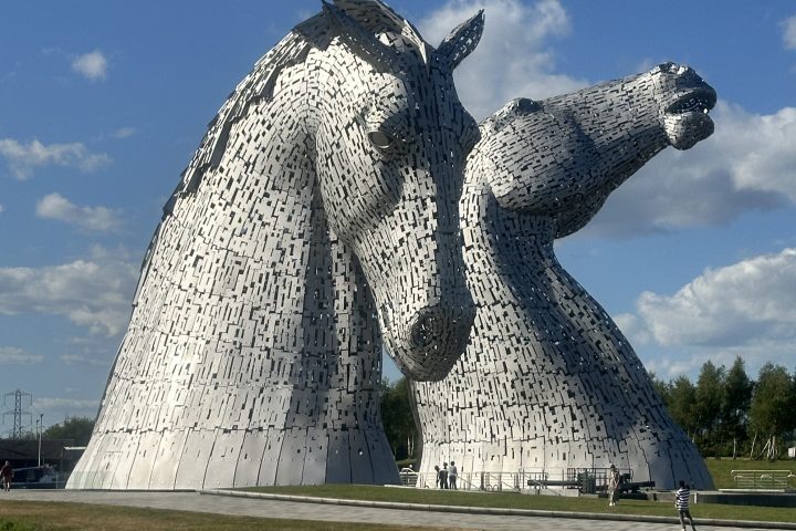 Two large horse head sculptures under a blue sky with clouds.