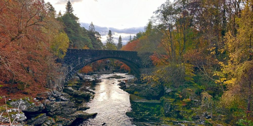 Stone bridge over a river in an autumn forest landscape.