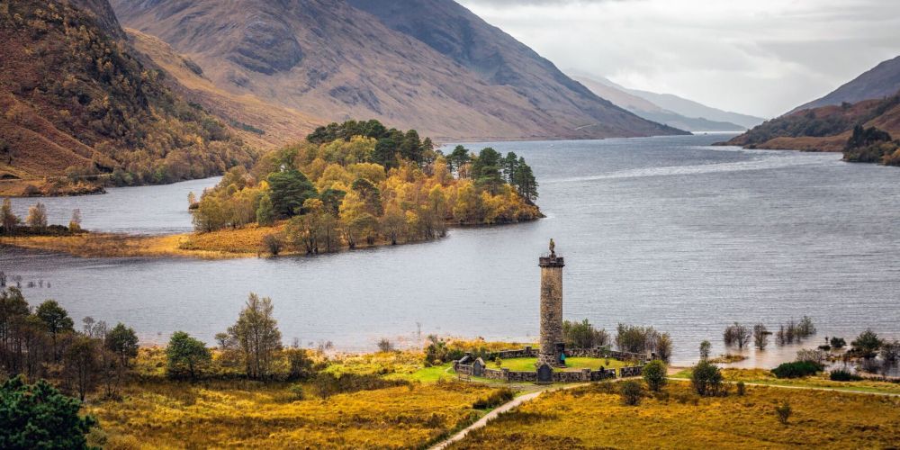 Scenic view of a valley, lake, and monument tower surrounded by mountains.